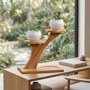 May include: A two-tiered bamboo plant stand with two small white ceramic pots, each holding a green succulent. The stand is on a wooden table near a window with a blurred outdoor view. A book and small vase are also on the table.