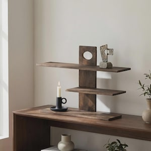 May include: A dark brown wooden wall shelf with three horizontal shelves and a vertical support. A black candle holder with a lit candle sits on a lower shelf. A small sculpture rests on the top shelf.