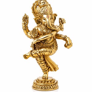 May include: A gold-colored statue of the Hindu deity Ganesha, depicted in a dynamic dancing pose. The statue features intricate details, including ornate jewelry, a large headdress, and multiple arms. The figure stands on a detailed circular base.