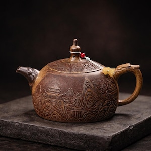 以下が含まれることがあります： 山と塔を含む詳細な風景デザインが施された茶色のセラミックティーポット。 ティーポットは、湾曲した注ぎ口と、ドラゴンの頭のデザインのハンドルを備えています。 赤と白のビーズが付いた小さな装飾要素が蓋に取り付けられています。