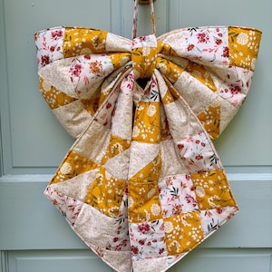 Grote herfststrik van patchwork, gequilt om aan de voordeur te hangen of in een krans met oranje, bruine en beige bloemen.