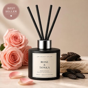 May include: A black reed diffuser with black reeds, a silver collar, and a white label that reads "Rose & Tonka." The diffuser is next to pink roses and tonka beans. The label also says "100 ml - Made in Scotland."