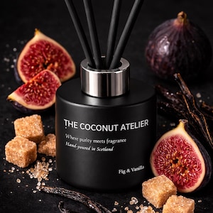 May include: A black diffuser bottle with a silver collar and black reeds. The bottle is labelled "THE COCONUT ATELIER" and "Fig & Vanilla." Fresh figs, vanilla pods, and sugar cubes are arranged around the bottle on a dark surface.