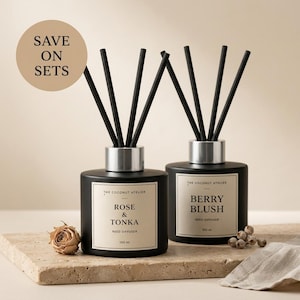 May include: Two black reed diffusers with silver collars and black reeds. One is labelled "Rose & Tonka", the other "Berry Blush". The text "Save on Sets" is in a circle in the upper left. Each bottle contains 100 ml.