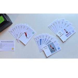 May include: A set of exercise cards with illustrations and instructions, including "Wall Push-Up" and "Squish Cross." A black box with "Movement" written on it and a card with "Movement Work Rules" are also present. The cards are designed for fitness activities.
