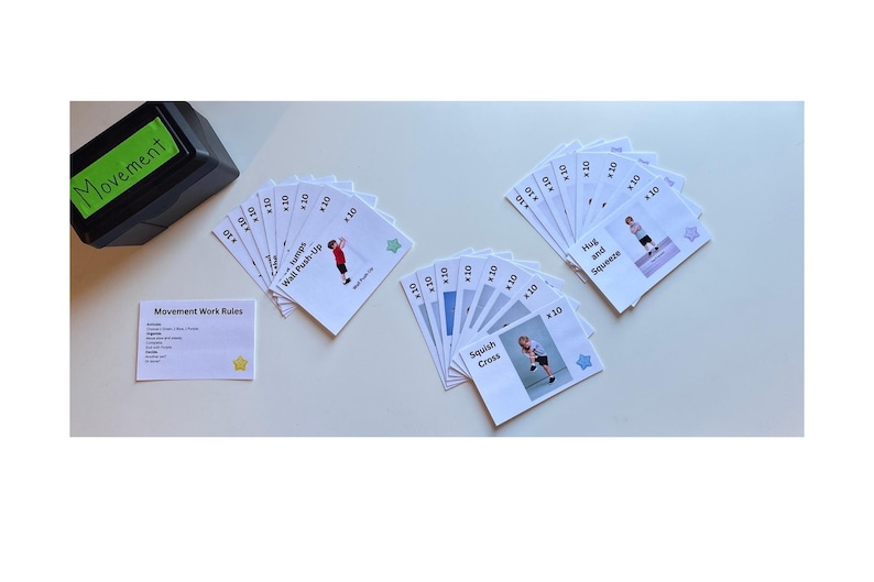 May include: A set of exercise cards with illustrations and instructions, including "Wall Push-Up" and "Squish Cross." A black box with "Movement" written on it and a card with "Movement Work Rules" are also present. The cards are designed for fitness activities.