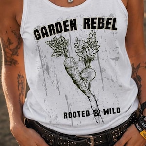 Könnte beinhalten: Weißes Tanktop mit dem Text "GARDEN REBEL" und einer Grafik einer Karotte und einer Rübe. Die Worte "ROOTED & WILD" stehen darunter. Das Tanktop wird mit schwarzen Shorts und einem schwarzen Gürtel getragen.