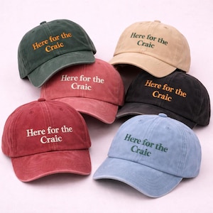 May include: Six baseball caps in different colours: green, beige, red, black, and blue. Each cap has the embroidered text "Here for the Craic" in a contrasting colour. A casual and stylish accessory for any outfit.