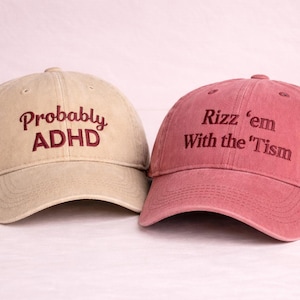 May include: Two baseball caps, one tan and one red. The tan cap has the embroidered text "Probably ADHD" in burgundy. The red cap has the embroidered text "Rizz 'em With the 'Tism" in burgundy. Both caps have a curved brim.
