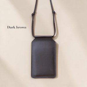 May include: A dark brown vertical rectangular phone pouch with a smooth finish and a matching thin shoulder strap. The pouch features a clean, minimalist design with visible stitching along the edges and the text Dark brown printed on the left.