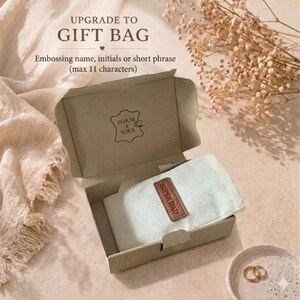 May include: A light brown cardboard gift box containing a light-colored fabric pouch with a brown leather tag embossed with the text SUPER DAD. The box lid features the text UPGRADE TO GIFT BAG, Embossing name, initials or short phrase (max 11 characters).
