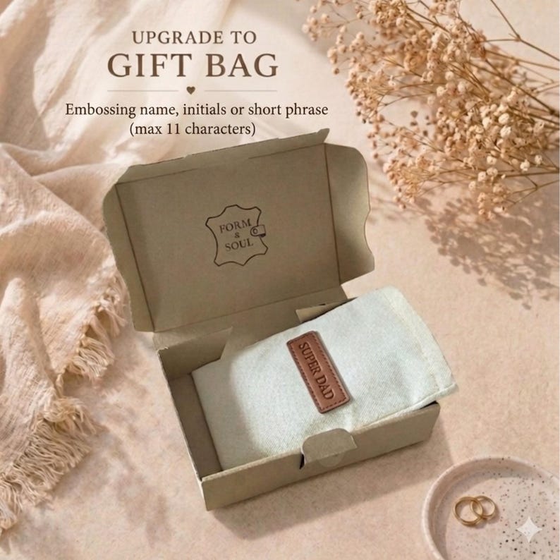 May include: A light brown cardboard gift box containing a light-colored fabric pouch with a brown leather tag embossed with the text SUPER DAD. The box lid features the text UPGRADE TO GIFT BAG, Embossing name, initials or short phrase (max 11 characters).
