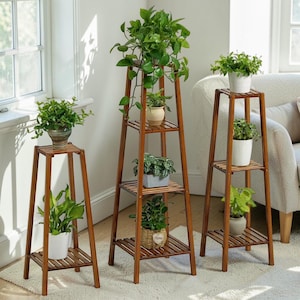 Op de afbeelding: Drie houten plantenstandaards van verschillende hoogtes, elk met meerdere planken met groene planten in potten. De standaards zijn gemaakt van warmbruin hout en staan in een goed verlichte kamer.