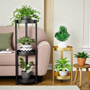 Puede incluir: Un soporte para plantas de metal negro con tres niveles, que sostiene plantas en macetas con follaje verde. También se ve un soporte para plantas de metal dorado con dos niveles, junto con un pequeño soporte para plantas de madera.