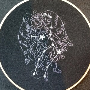 May include: A black embroidery hoop with a white embroidered constellation design. The constellation is outlined in white thread and has white stars.