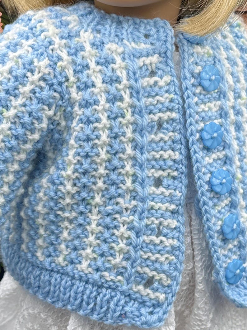 May include: A light blue and white knitted cardigan with a textured pattern. The cardigan features a round neckline, long sleeves, and is fastened with three light blue flower-shaped buttons. The garment is designed for a child.