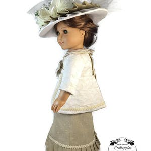 May include: A doll wearing a white jacket with a beige skirt and a white hat with a large white flower and a white feather. The doll is standing on a white background. The doll is wearing a white jacket with a beige skirt and a white hat with a large white flower and a white feather. The doll is standing on a white background.