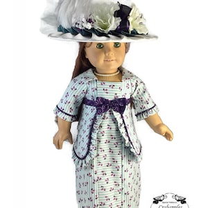 May include: A doll wearing a light blue and white striped dress with a floral pattern. The dress has a purple sash and a matching jacket. The doll is wearing a white hat with a white feather and white and purple flowers.