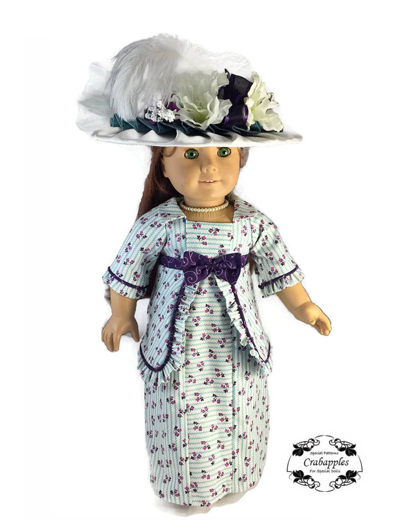 May include: A doll wearing a light blue and white striped dress with a floral pattern. The dress has a purple sash and a matching jacket. The doll is wearing a white hat with a white feather and white and purple flowers.