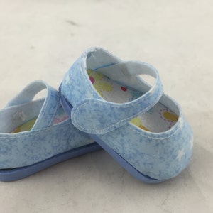 May include: A pair of light blue baby shoes with a white star pattern and a white lining with colorful flowers. The shoes have a velcro strap closure.