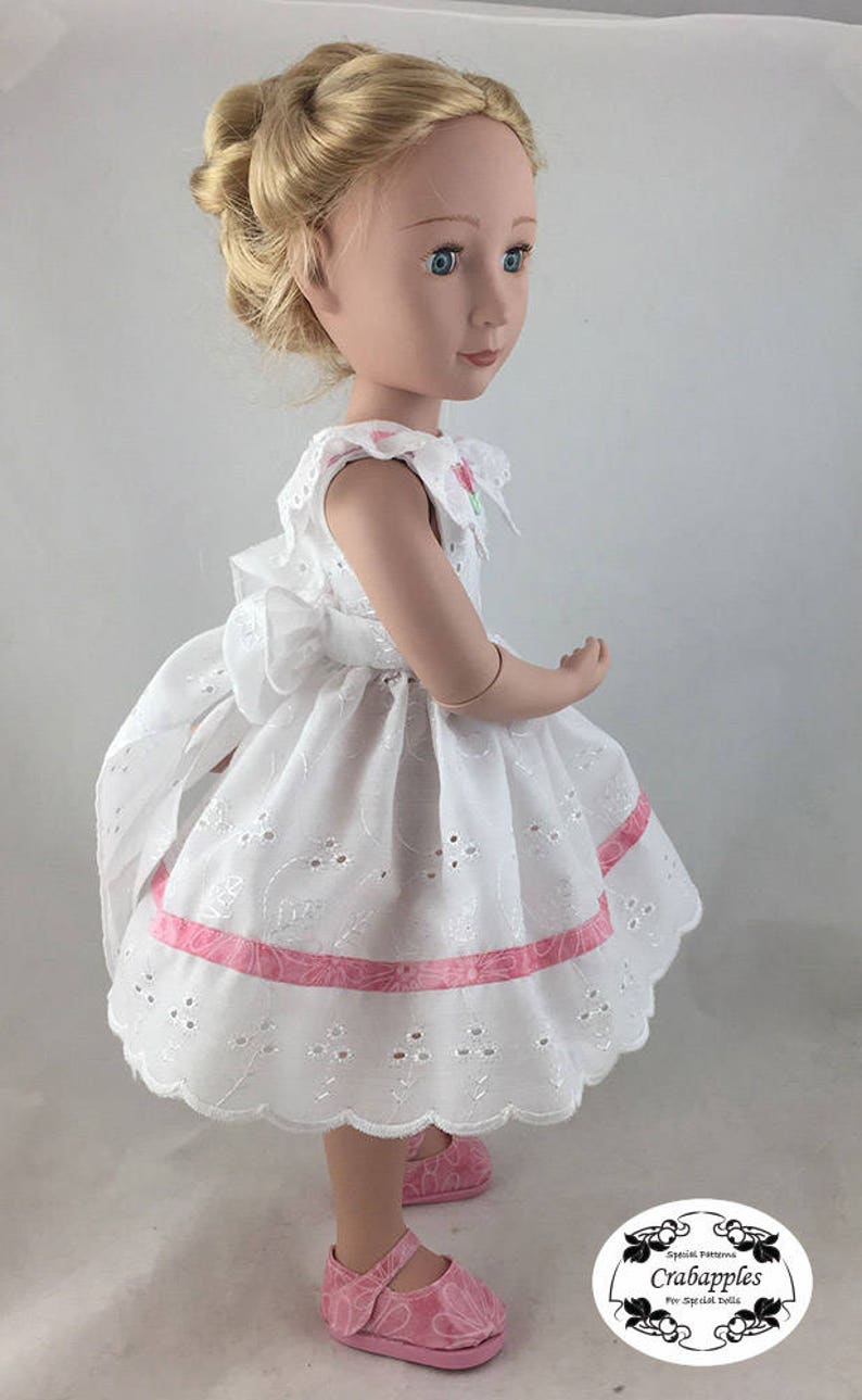 May include: A white eyelet dress with pink ribbon trim and a scalloped hem. The dress is worn by a doll with blonde hair and blue eyes. The doll is wearing pink shoes. The image includes the text "Special Patterns Crabapples for Special Dolls".