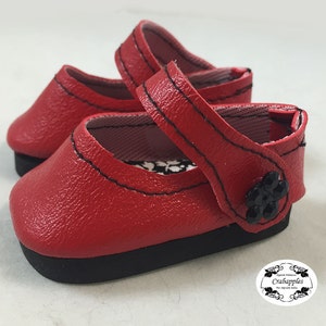 May include: Red leather doll shoes with black stitching and a black flower embellishment.