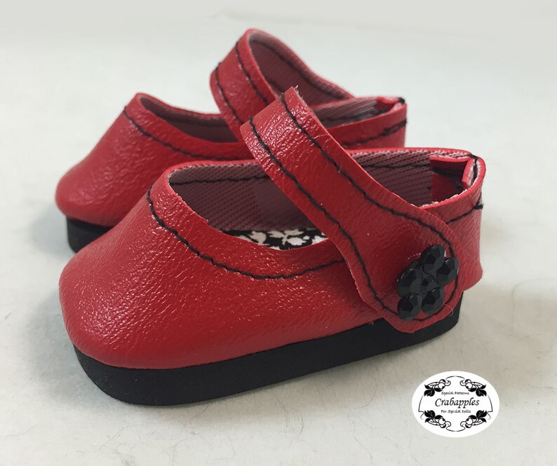 May include: Red leather doll shoes with black stitching and a black flower embellishment.