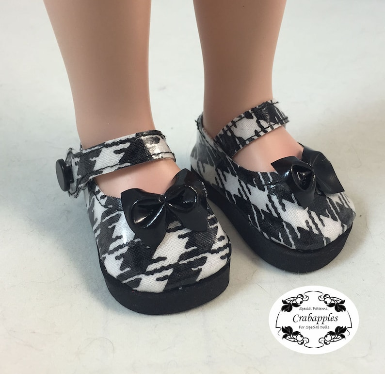 May include: Black and white houndstooth doll shoes with black bows and a black buckle. The shoes are made for dolls.