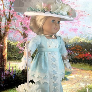 May include: A doll wearing a light blue dress with white lace trim and a white hat with a white feather and flowers. The doll is holding a white parasol with a white flower on top. The doll is standing in a garden setting.