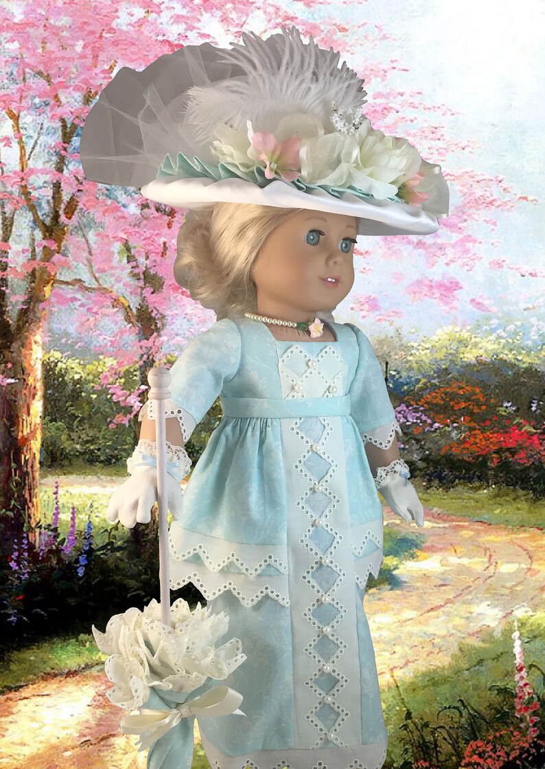 May include: A doll wearing a light blue dress with white lace trim and a white hat with a white feather and flowers. The doll is holding a white parasol with a white flower on top. The doll is standing in a garden setting.