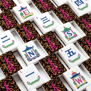 May include: A collection of mahjong tiles featuring white faces with blue, green, and pink printed characters and pagoda designs, alternating with dark brown and black tortoiseshell-patterned backs marked with a large pink letter A.