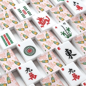 May include: A close-up of a Mahjong set with white tiles featuring various symbols and numbers in red, green, and black. The background shows a pattern of champagne bottles and glasses on a pink and white striped background.