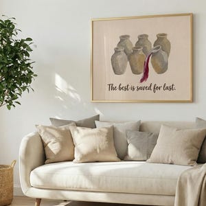 May include: A framed wall art print featuring a group of six beige ceramic jars, with one jar pouring out dark red liquid. Below the jars, the text reads, The best is saved for last. The artwork is displayed in a thin gold frame on a white wall.