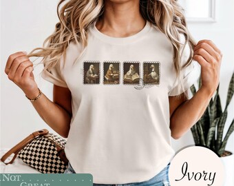 May include: An ivory short-sleeve t-shirt featuring a graphic print of four rectangular postage stamp designs. Each stamp depicts a duck engaged in different activities, including writing, reading, and working, with a circular postmark stamp.