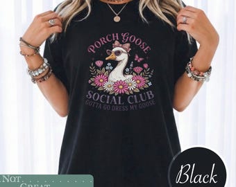 May include: A black t-shirt featuring a graphic of a white goose wearing pink sunglasses and a pink bow. The goose is surrounded by pink and white flowers and butterflies. The text reads PORCH GOOSE SOCIAL CLUB GOTTA GO DRESS MY GOOSE.
