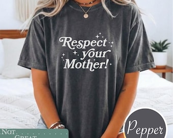 May include: A charcoal gray short-sleeve t-shirt with a vintage-wash finish. The front features white text that reads Respect your Mother! surrounded by small star icons. The shirt has a crew neckline and a relaxed fit, providing a casual look.