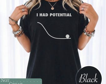 May include: A black short-sleeved t-shirt featuring the white text I HAD POTENTIAL above a white graphic of a curved line representing a slope with a small circle at the bottom, illustrating a physics concept of potential energy in a simple design.