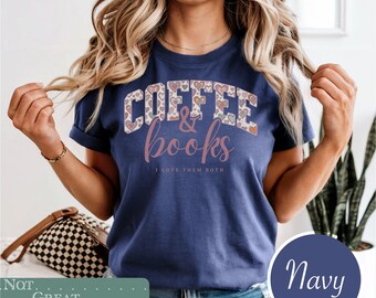 May include: A navy blue short-sleeve t-shirt featuring the text COFFEE & books in a stylized font. The word COFFEE is filled with a pattern of small hearts in various colors, while the word books is in a script font. Below, the text reads I LOVE THEM BOTH.