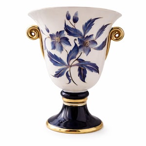 Op de afbeelding: Een witte keramische vaas met blauwe bloemmotieven en gouden accenten. De vaas heeft een brede bovenkant, twee gouden handvatten en een donkerblauwe voet met gouden rand. Het bloemmotief omvat blauwe bloemen en bladeren.