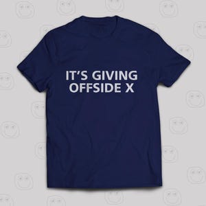 Puede incluir: Una camiseta azul marino con el texto blanco "IT'S GIVING OFFSIDE X". Esta camiseta de cuello redondo es perfecta para un look casual. El texto está centrado en la parte delantera de la prenda.