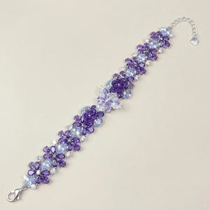 May include: A bracelet with a floral design, incorporating purple, light blue, and clear crystals. The silver-tone chain includes a heart-shaped charm and a lobster clasp. The bracelet features flower and leaf details.