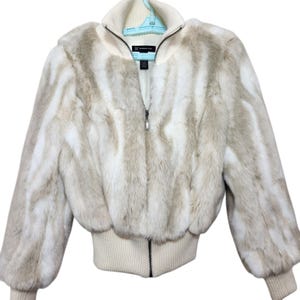 May include: A faux fur bomber jacket in cream and light brown vertical stripes. The jacket has a ribbed knit collar, cuffs, and hem, with a full-length zipper closure. The jacket is hanging on a light blue hanger.