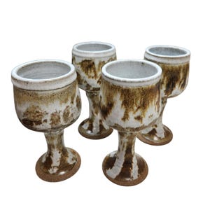 May include: Four handmade ceramic wine goblets. Each goblet has a white interior and a brown and white exterior with a unique, organic pattern. The stem and base are brown, and the rim is white.