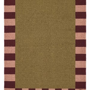 Può includere: Un tappeto rettangolare con un pannello centrale in tinta unita verde oliva, circondato da un'ampia bordura a strisce verticali alternate in rosa polvere e bordeaux scuro. L'angolo in basso a destra presenta un logo circolare con il testo BLR.