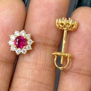 May include: A pair of gold stud earrings featuring a central round-cut vibrant pink gemstone surrounded by a halo of small clear white stones. One earring is shown from the front, while the other is displayed from the side, revealing the post.