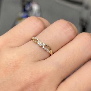Op de afbeelding: Een gouden ring met een delicaat, gedraaid bandontwerp dat in het midden kruist. De band is geaccentueerd met een reeks kleine, heldere, rondgeslepen stenen die in het oppervlak zijn ingelegd, wat zorgt voor een subtiele schittering op de dunne band.