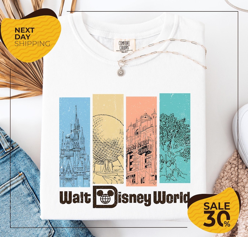 a white t-shirt with a graphic design depicting various landmarks and buildings from Walt Disney World, including the Eiffel Tower, the castle, and the roller coaster. The t-shirt is displayed on a white background, and there are yellow and black sale tags indicating a 30% discount.