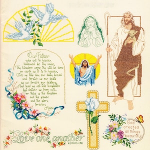 Op de afbeelding: Een kruissteekpatroonblad met religieuze motieven, waaronder twee witte duiven, een biddende figuur, een herder met een lam, een kruis met een blauwe roos en de tekst van het Onze Vader. Florale accenten en vlinders sieren de ontwerpen.