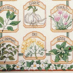 May include: Cross-stitch sampler depicting various herbs such as bay laurel, garlic, chives, spearmint, dill, and basil. Each herb is labelled within a decorative frame, with detailed botanical illustrations. The sampler is on a cream-coloured fabric.