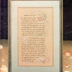 May include: Framed cross-stitch artwork featuring the poem "Footprints in the Sand." The text is in a handwritten style, with decorative elements of seashells and plants. The frame is a light brown color.